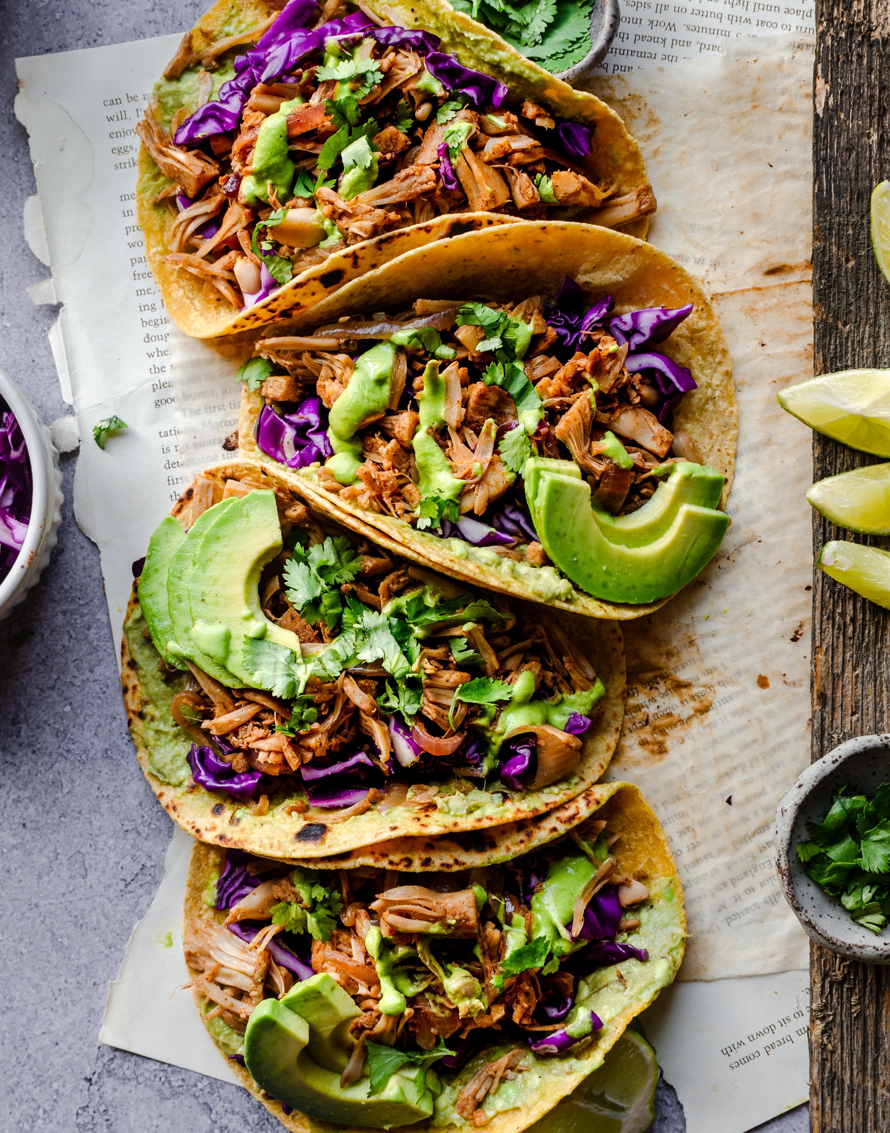 Sweet chili jackfruit tacos topped with toasted peanuts and cilantro, served on a rustic wooden board with lime wedges.