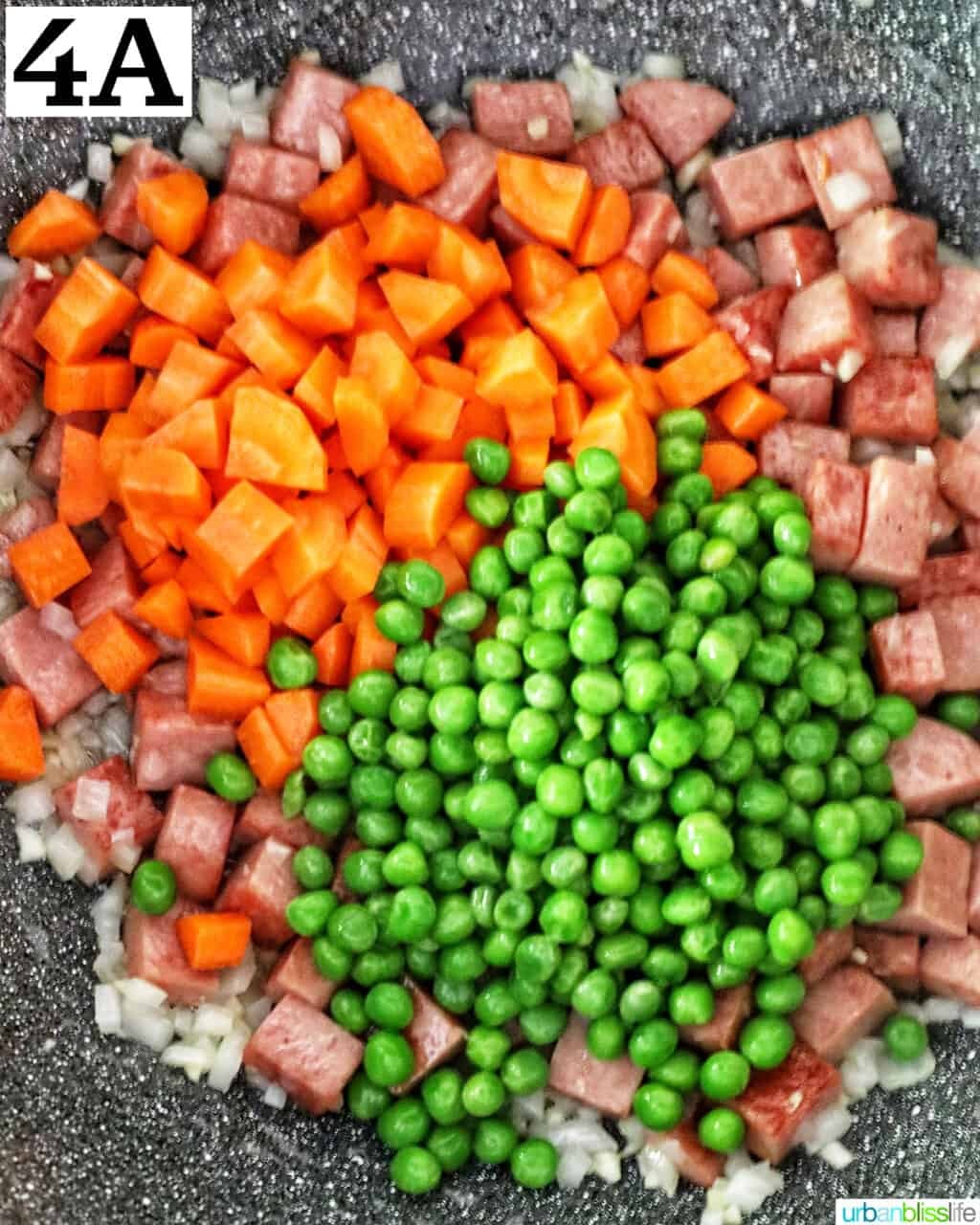 A bowl of fluffy boiled rice with bright green peas and orange carrots.