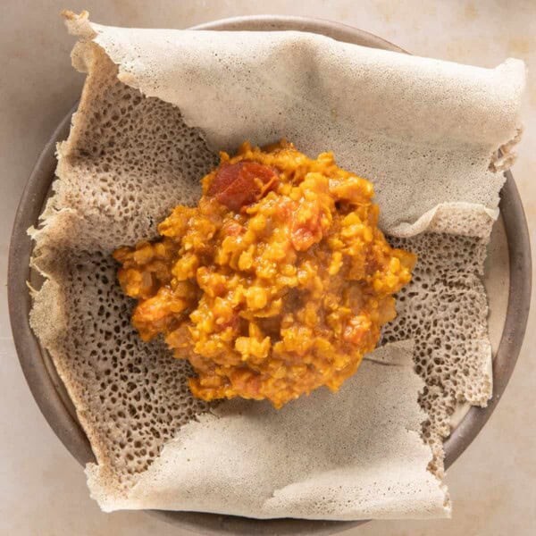 A steaming plate of injera topped with a generous serving of shiro wat, garnished with fresh herbs.