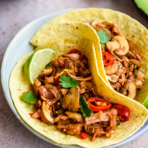 Mushroom and jackfruit tacos topped with cilantro and lime wedges