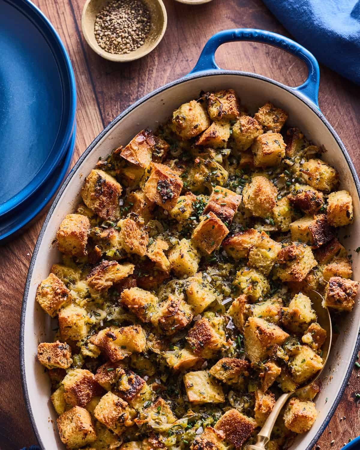 rustic golden brown savory herb stuffing in a large baking dish with fresh herbs
