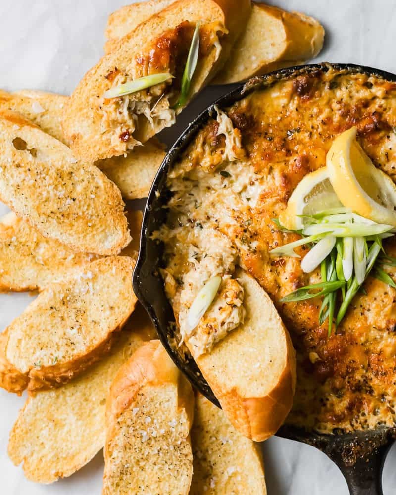 hot baked crab dip with golden melted cheese served on a rustic board with crackers
