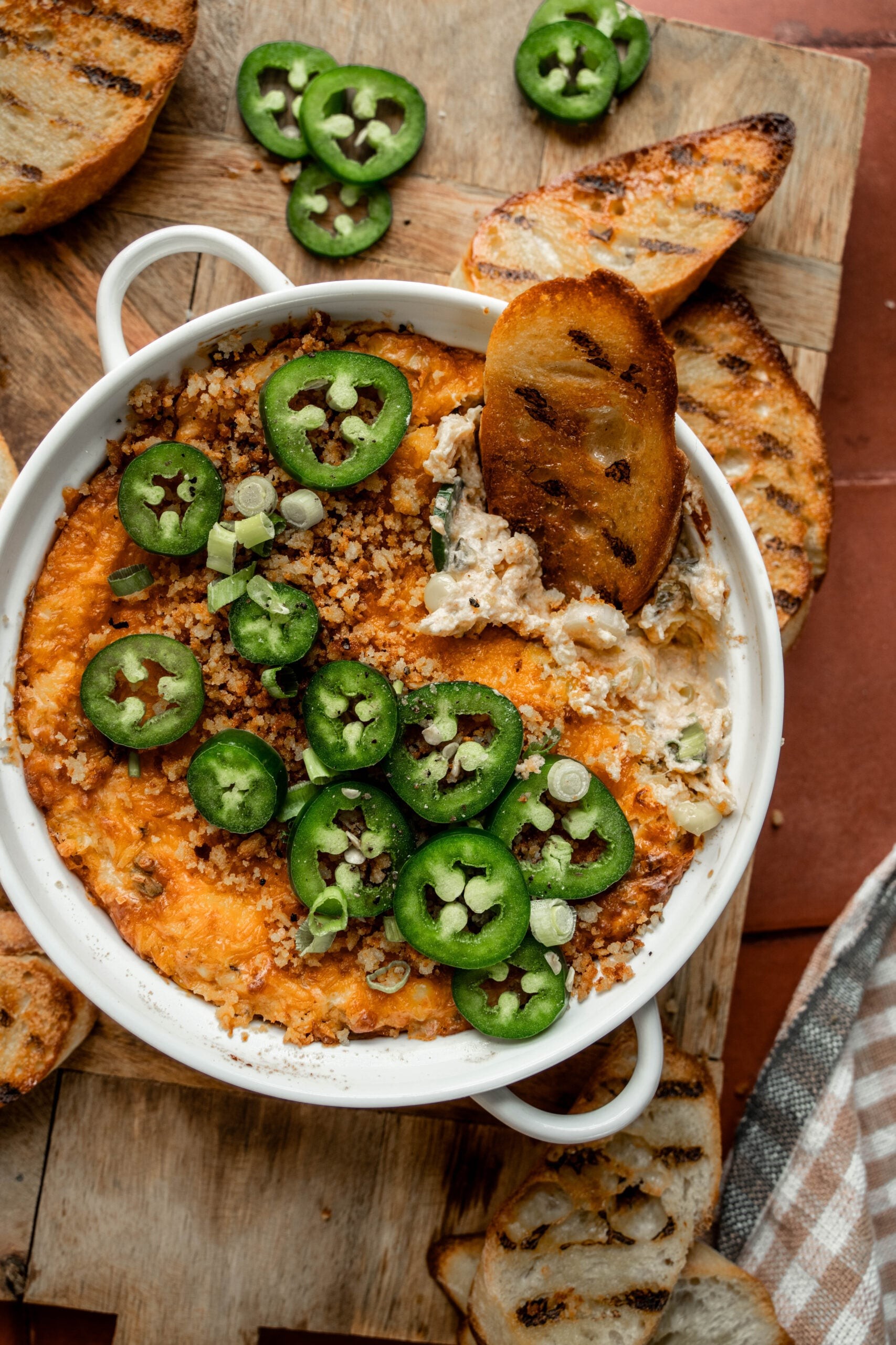 Creamy baked jalapeño popper dip in a rustic dish with crackers and fresh jalapeños