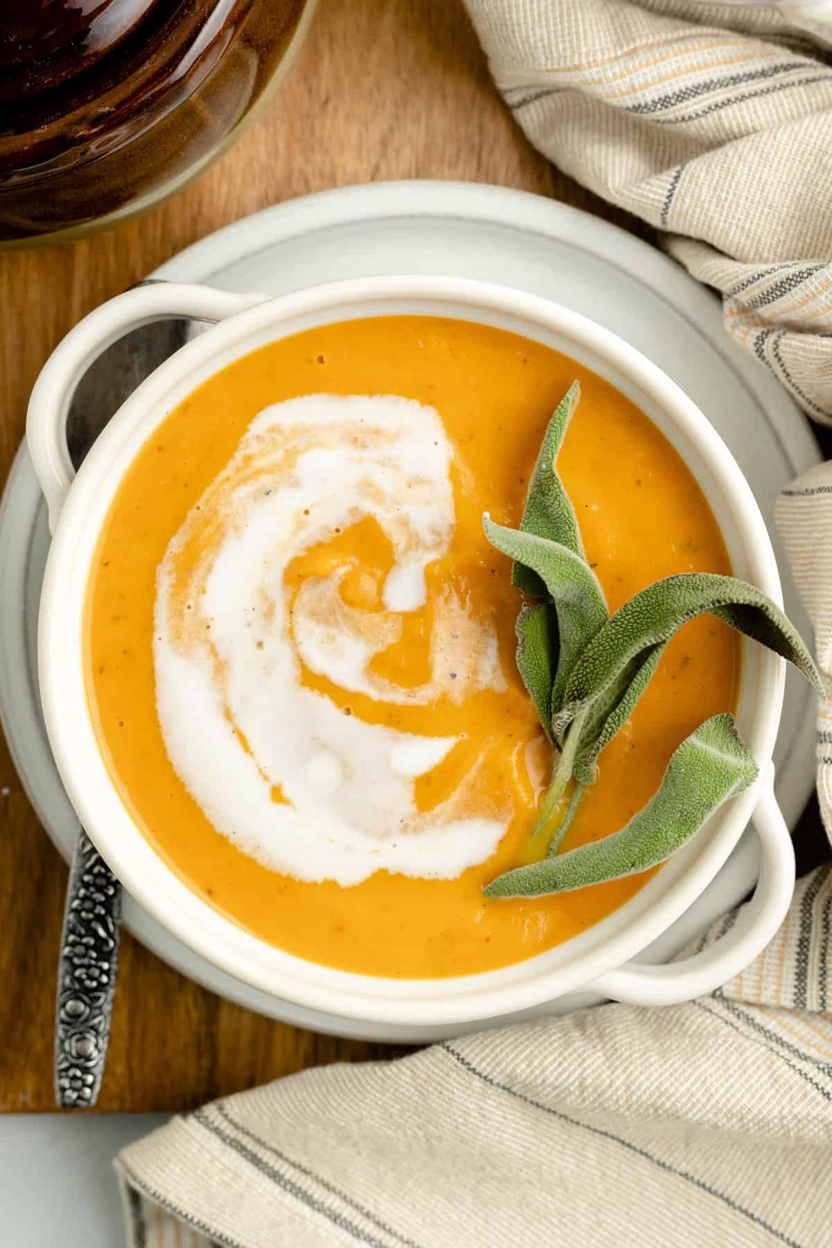 A rustic bowl of creamy pumpkin soup garnished with fresh sage leaves and a drizzle of brown sugar