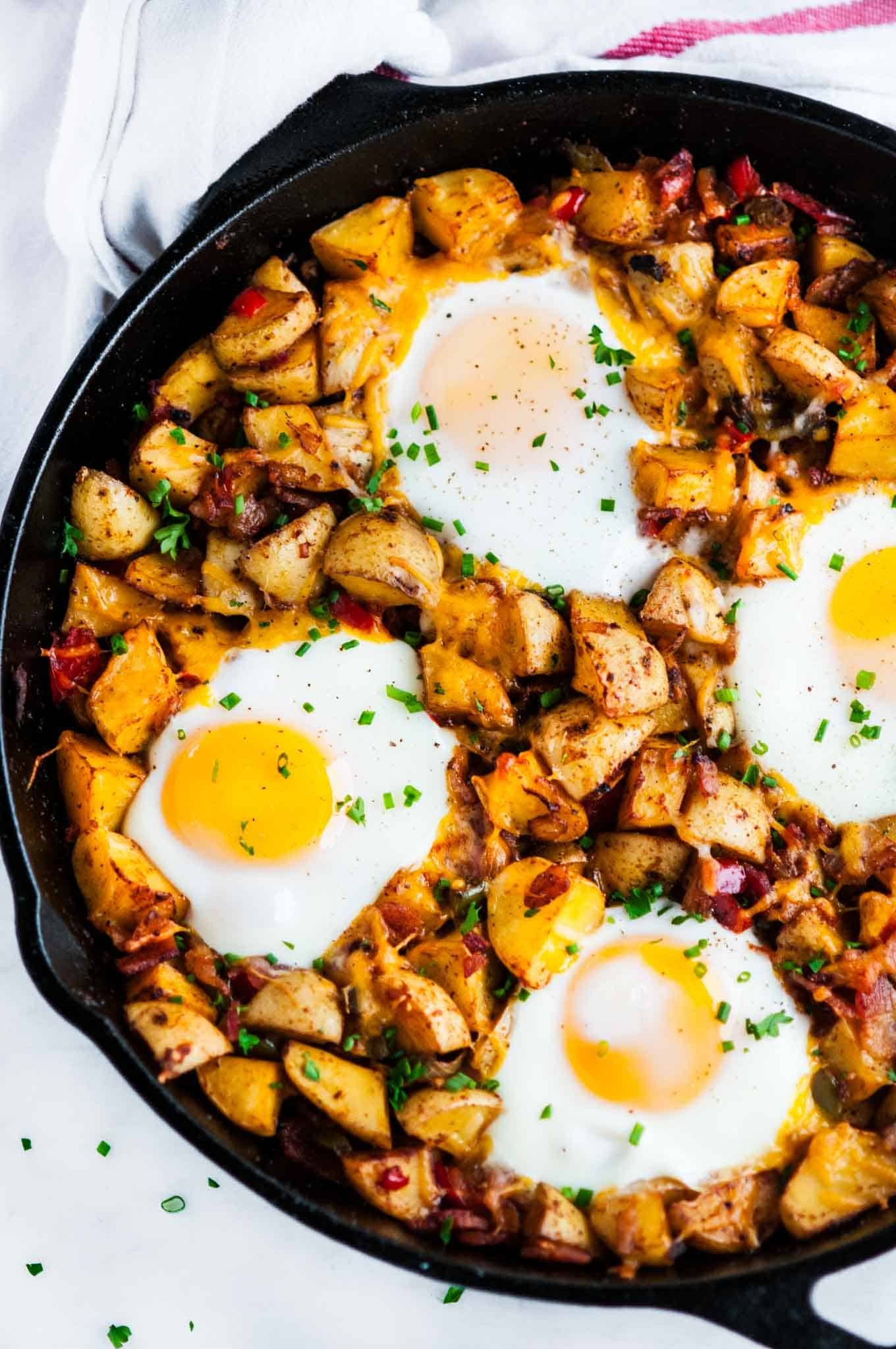 vibrant cast iron skillet with egg-loaded sunrise hash, golden crispy potatoes, runny yolks, fresh herbs