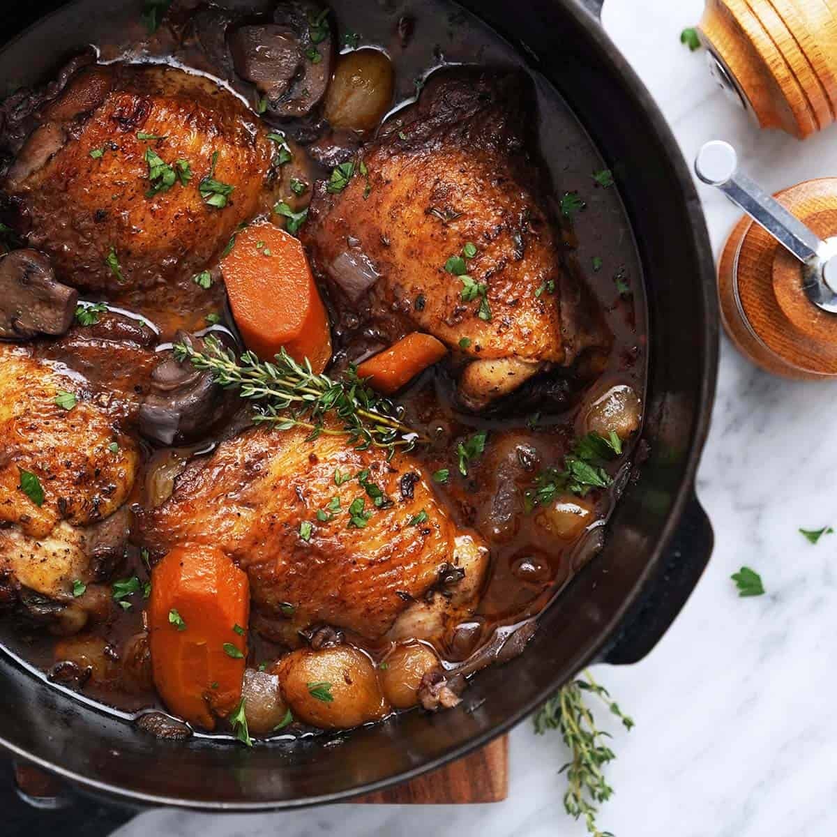 A rustic autumnal scene, featuring a cast iron Dutch oven bubbling with a coq au vin stew. The aroma is inviting and rich.  There is a red wine bottle in the background. Some fresh parsley is sprinkled over the top of the stew.