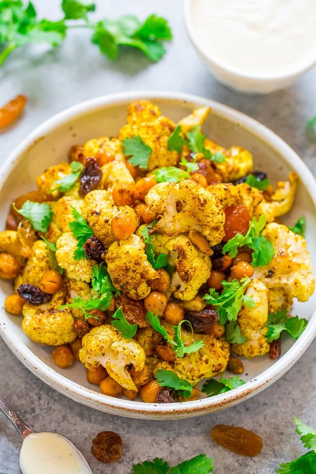 A colorful bowl of curried cauliflower and chickpeas, garnished with fresh cilantro