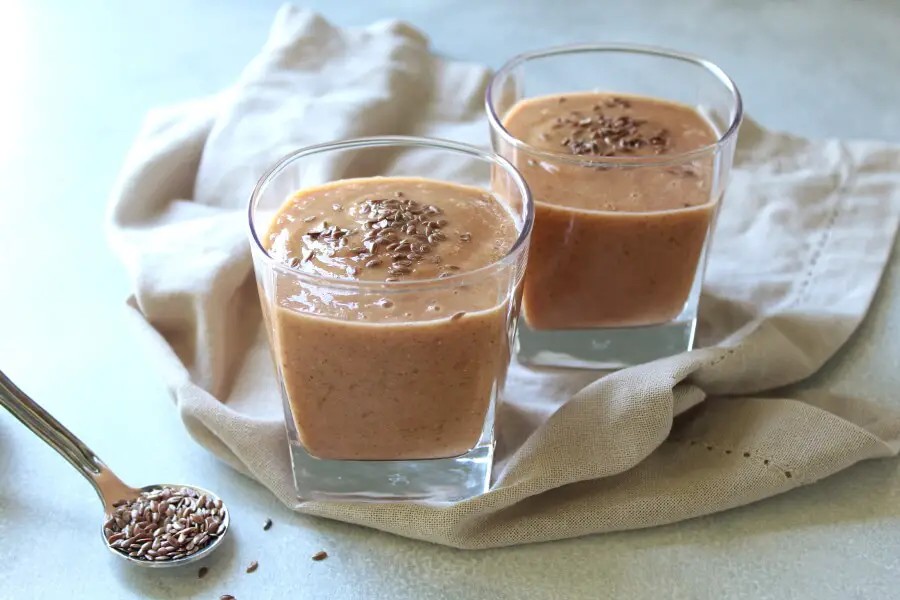 A glass of flaxseed smoothie with flax seeds and fresh berries on the side