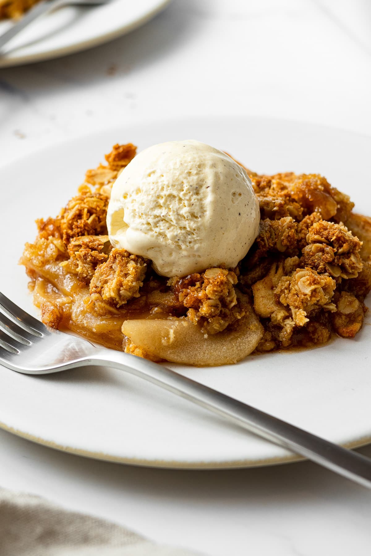 A golden-brown apple crisp bubbling in a baking dish, with a scoop of vanilla ice cream on top
