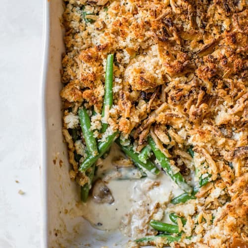 Classic green bean casserole with a golden brown crispy crumb topping, served on a rustic holiday table setting.
