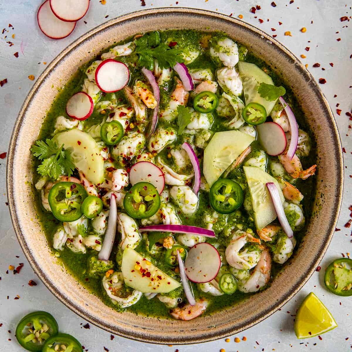 A vibrant bowl of ceviche with chilies, garlic, and cilantro, garnished with lime wedges.