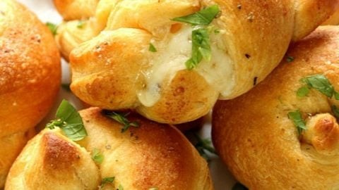 Golden brown garlic knots stuffed with melted cheese on a rustic wooden board, garnished with fresh parsley, perfect for a holiday party.