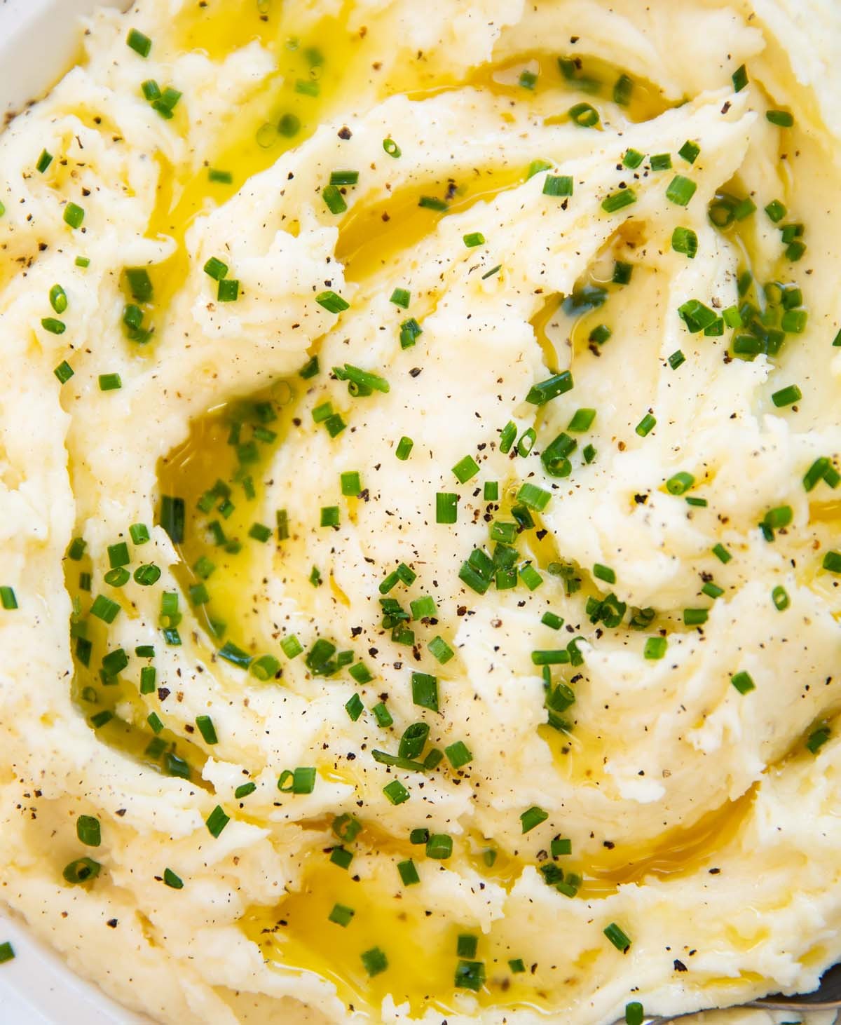Close-up of creamy mashed potatoes with a golden butter swirl on top, garnished with fresh chives