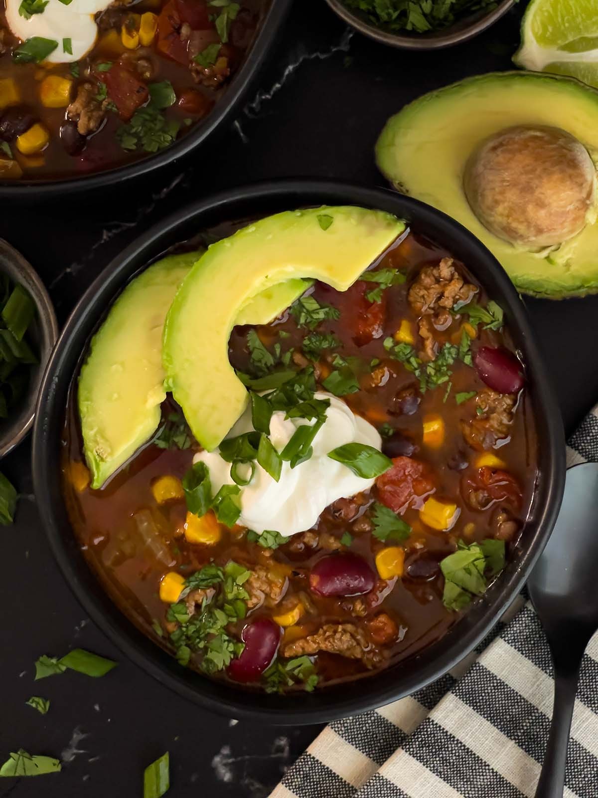 hearty bowl of smoky taco beef soup with toppings, cozy setting