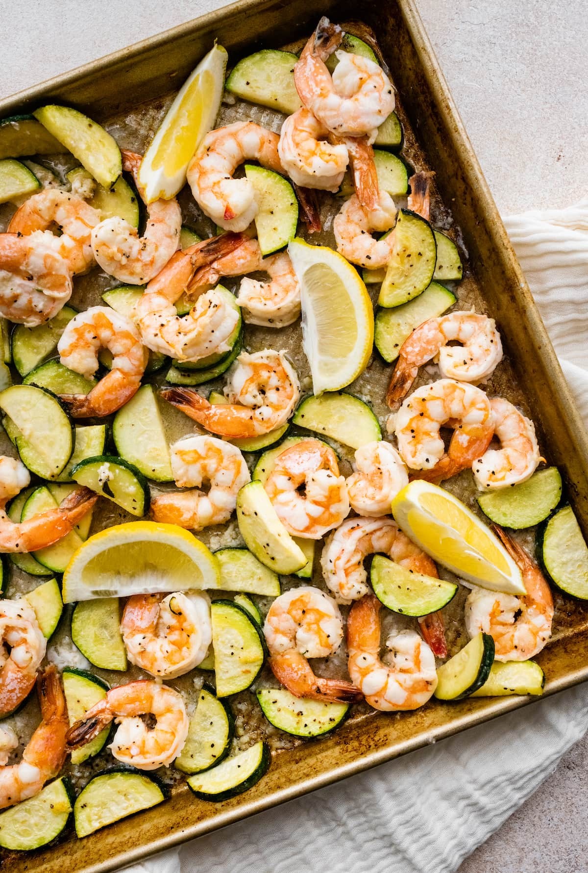 Sheet pan of sizzling shrimp scampi with zucchini, garlic, and herbs, garnished with lemon wedges