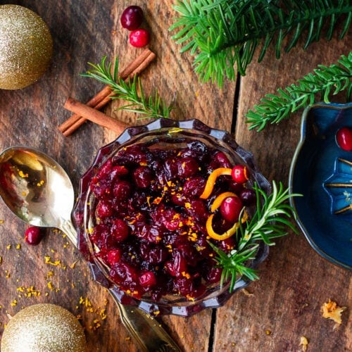 Vibrant homemade cranberry sauce in a rustic bowl, garnished with orange zest and fresh cranberries, set on a festive holiday table