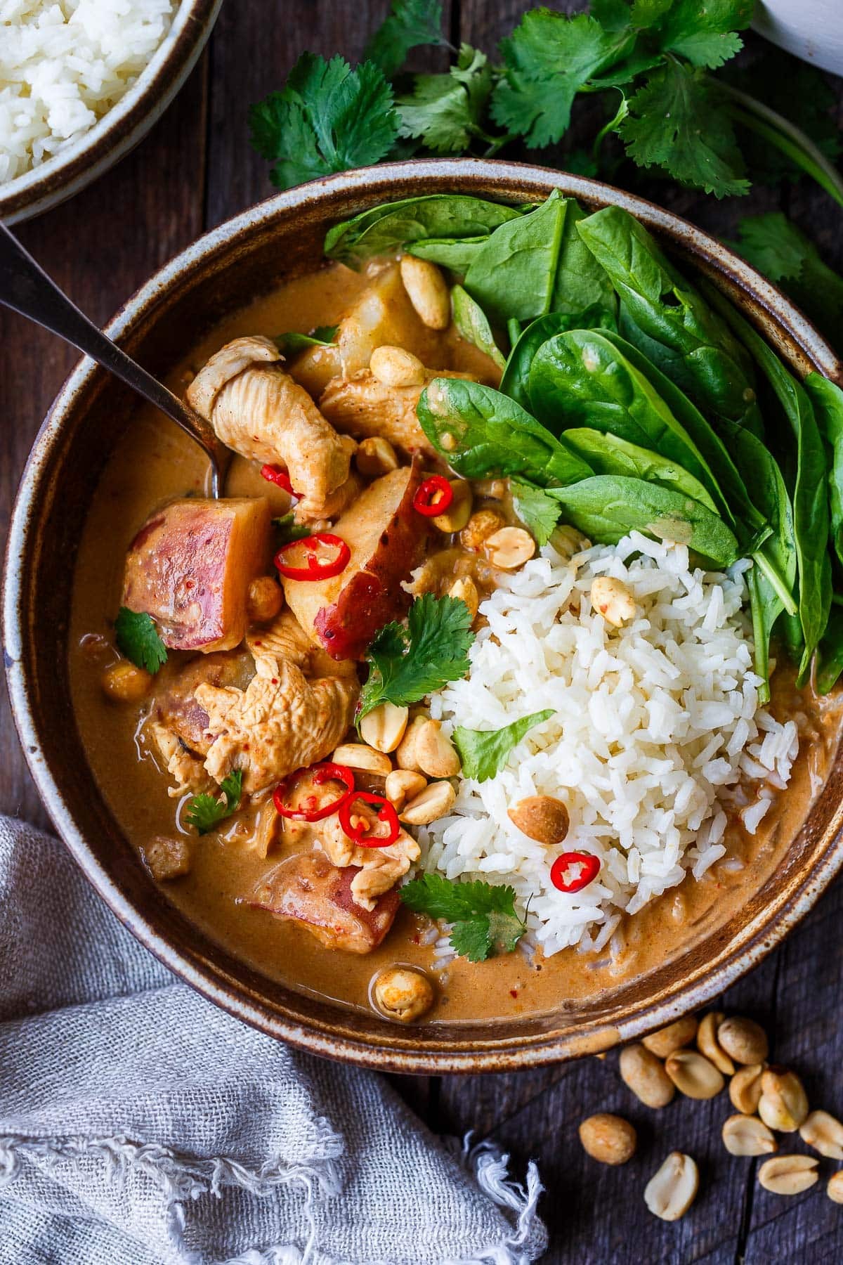 A steaming bowl of jasmine rice topped with rich Massaman curry, garnished with fresh cilantro and peanuts.