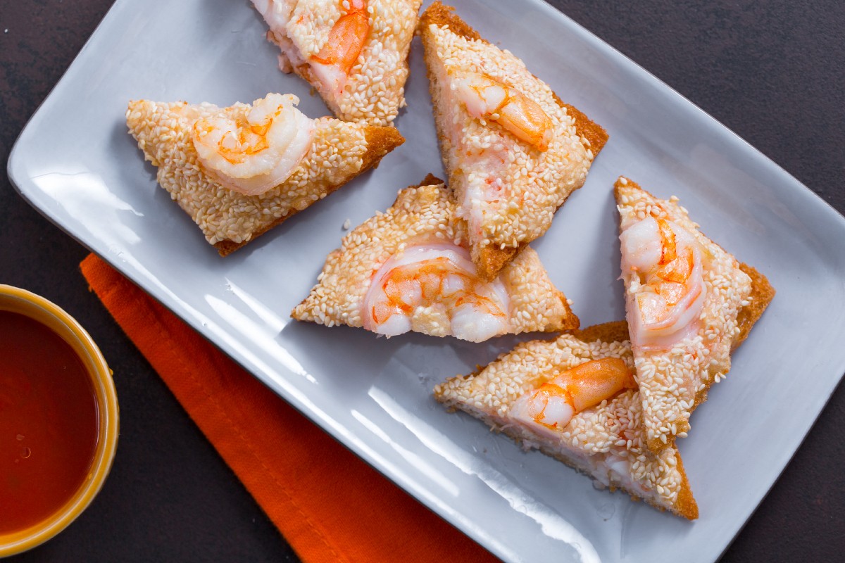 Golden fried sesame shrimp toast appetizer on a platter with dipping sauce