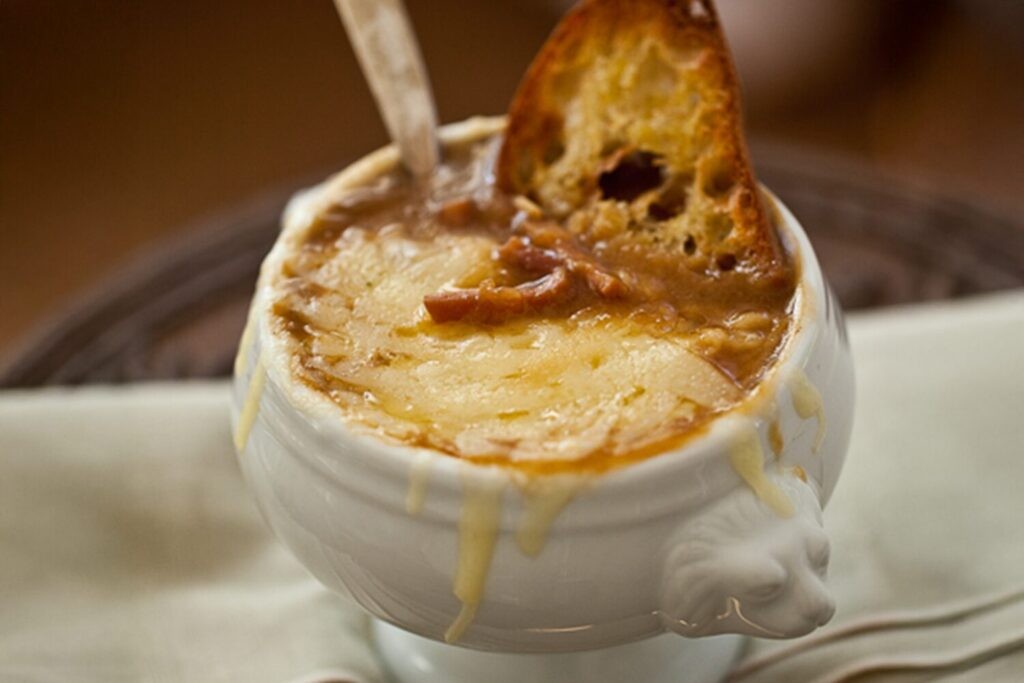 Rustic bowl of rich caramelized onion soup with crusty bread and melted gruyere cheese, steam rising