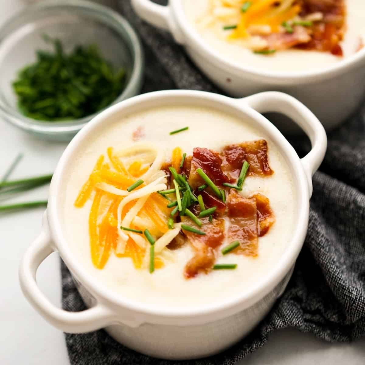A rustic bowl of creamy potato and bacon soup, garnished with fresh chives.