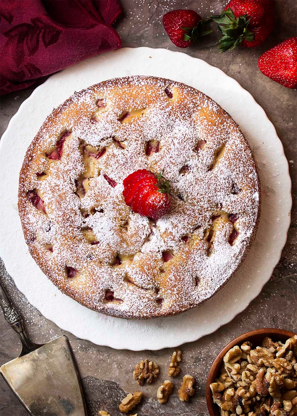 A slice of strawberry walnut cake on a plate, with fresh strawberries around it