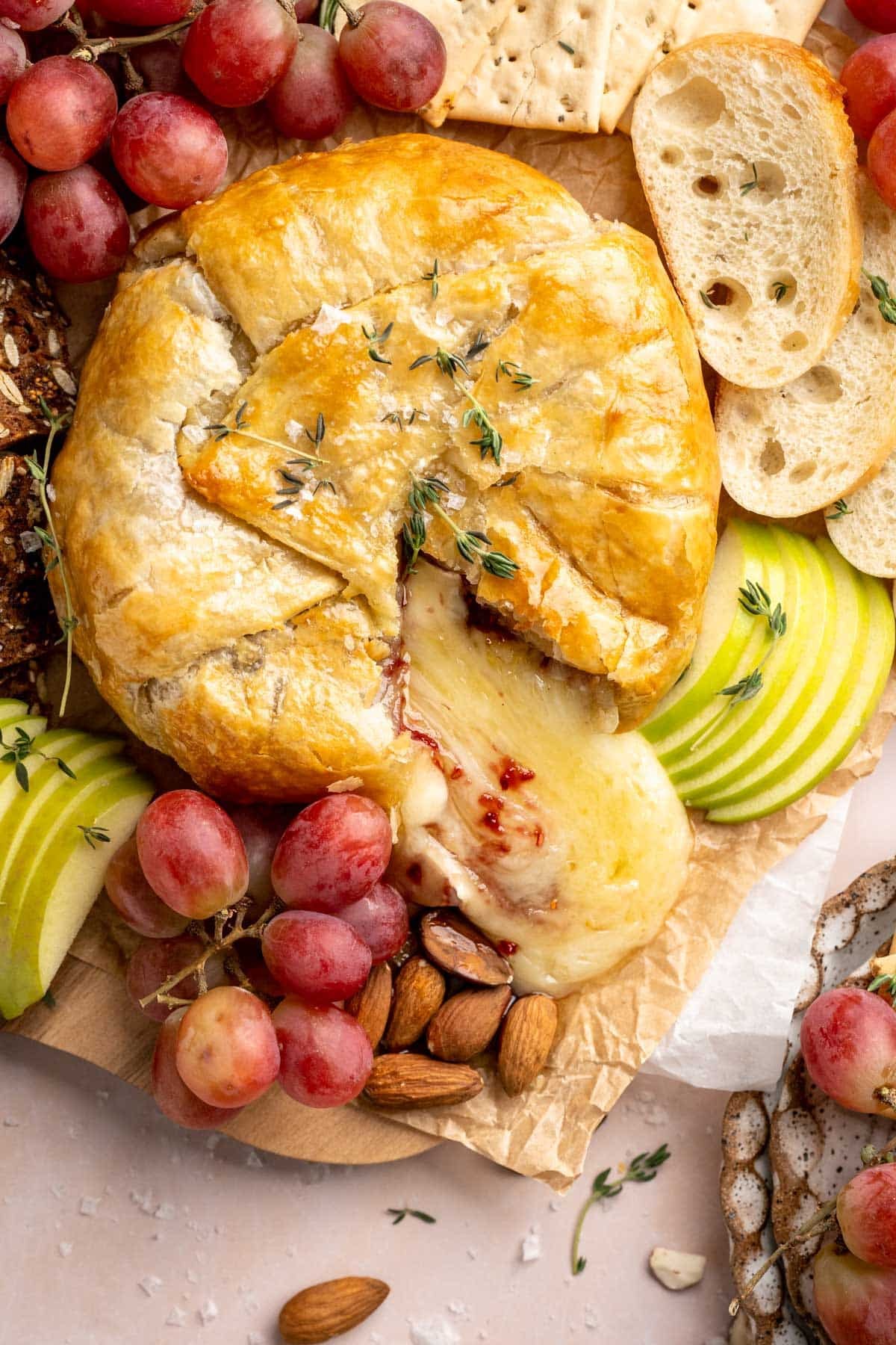 beautifully golden baked brie in puff pastry with fruit and crackers on a serving board
