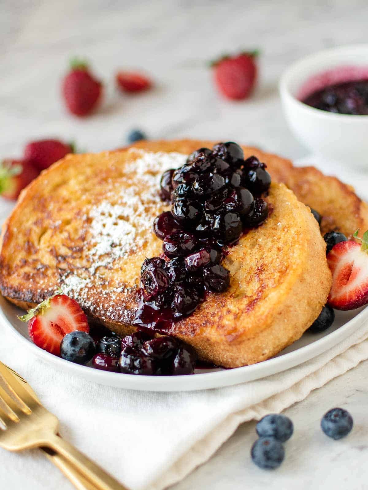 golden brown slices of french toast with a dollop of sour cream and berries on a plate