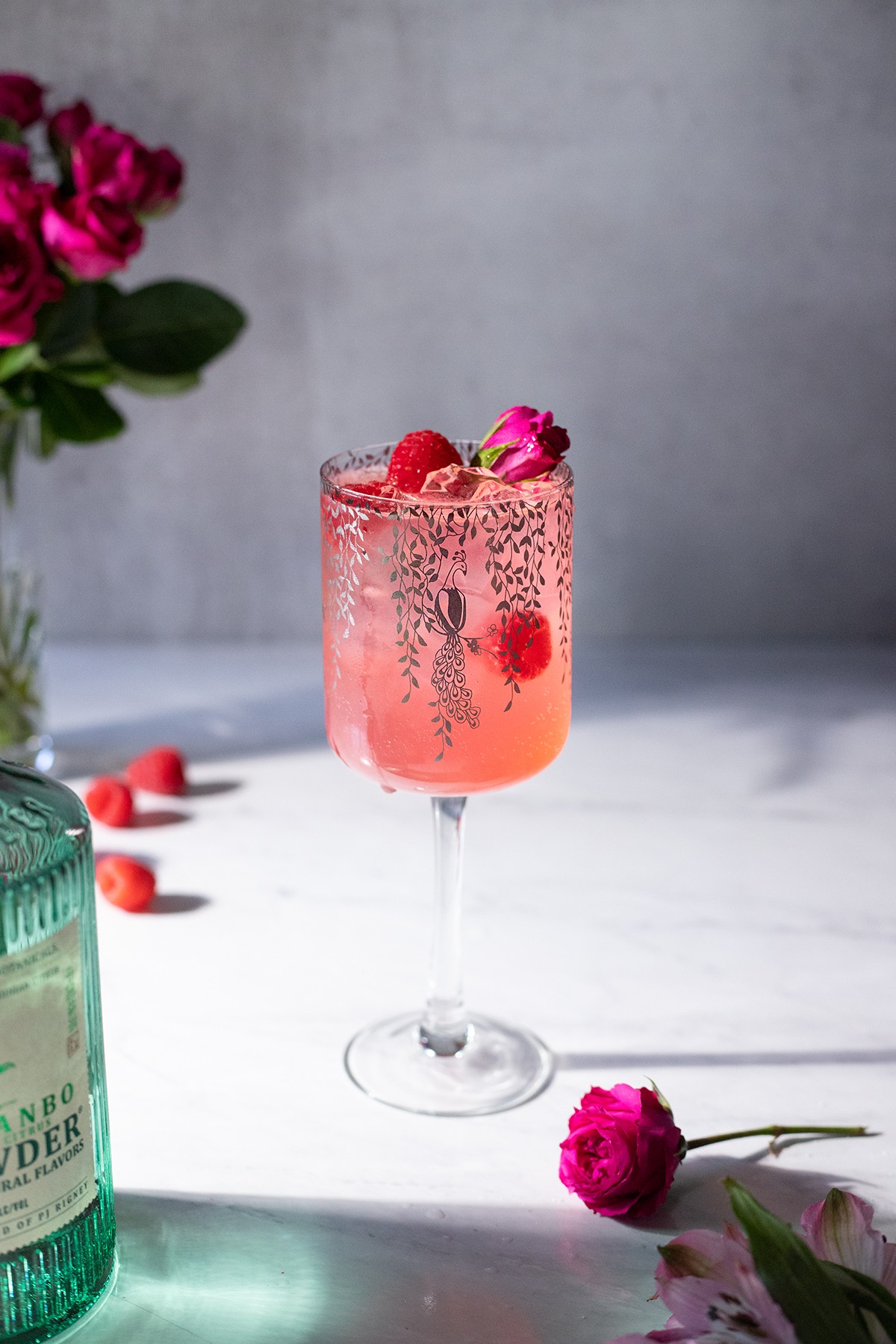 Close-up shot of a vibrant pink Raspberry Rose Smoothie in a glass with fresh raspberries and rose petals garnishing it.