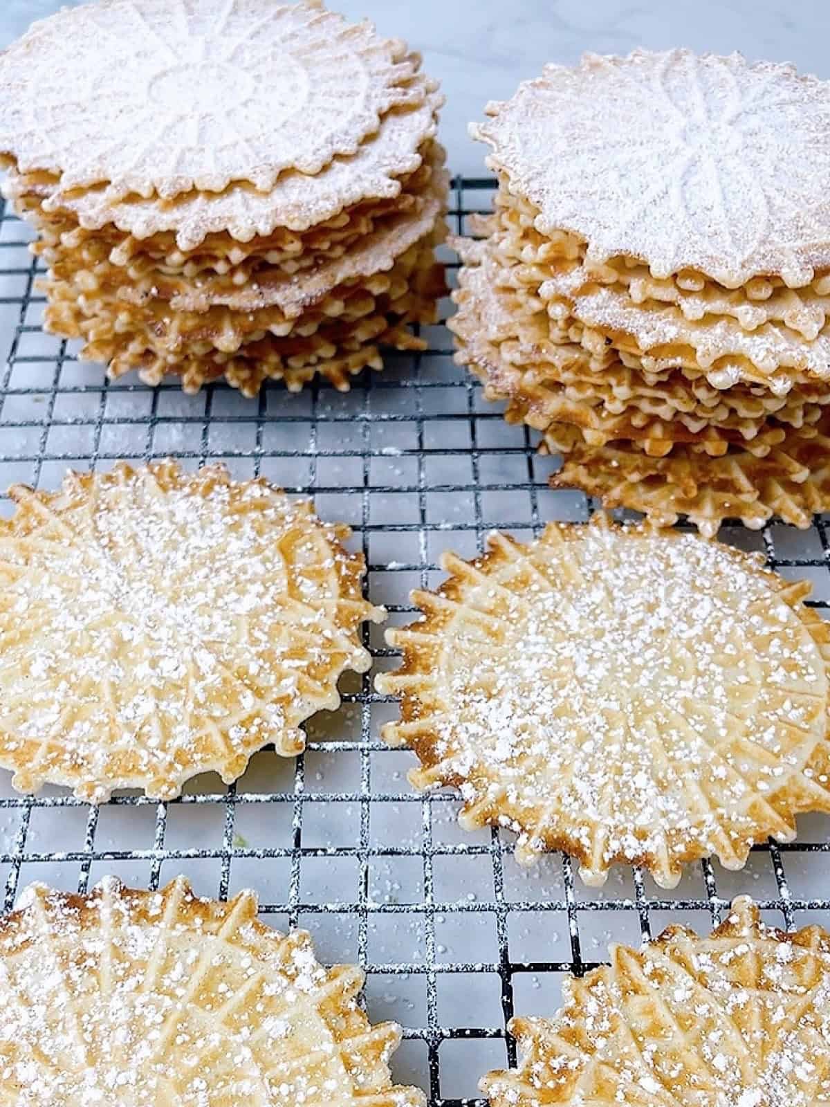 close-up of anise pizzelle cookies arranged on a plate, dusted with powdered sugar