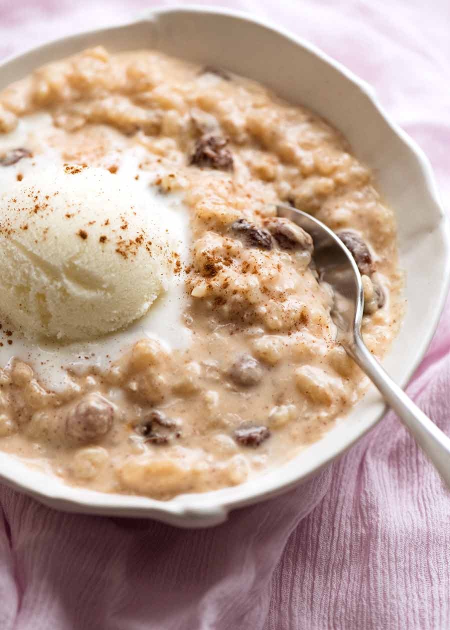 Warm baked rice pudding in a ceramic dish with a spoon, garnished with cinnamon