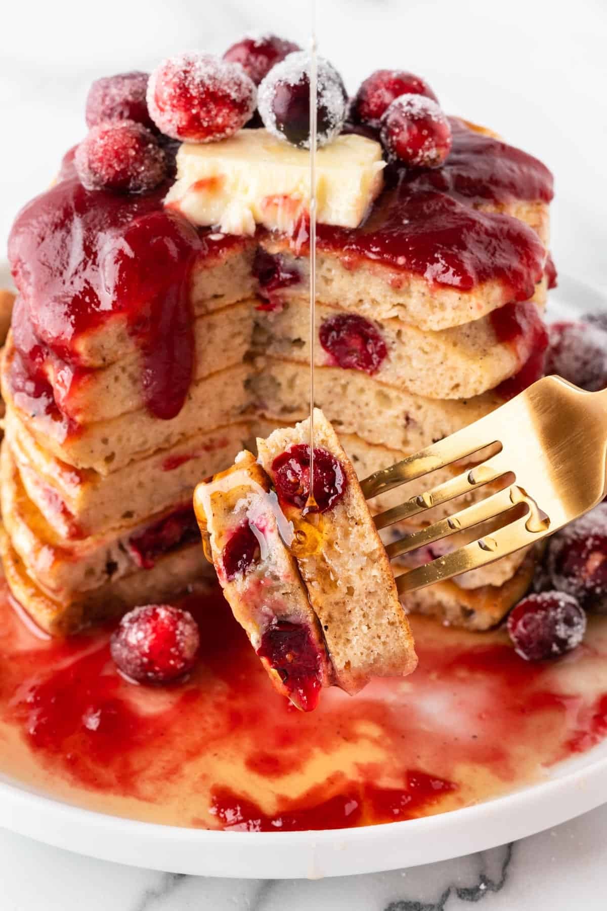 A stack of fluffy cranberry pancakes with a dollop of whipped cream and a sprinkle of powdered sugar, shot from above