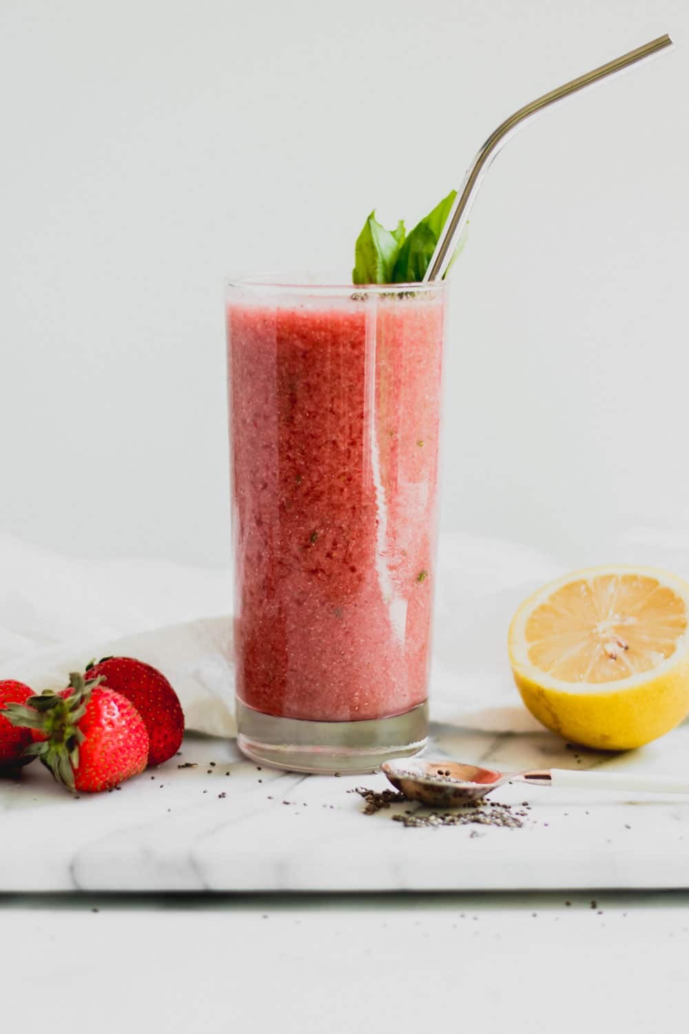 bright and refreshing basil strawberry smoothie in a glass with fresh basil leaves and strawberries around it