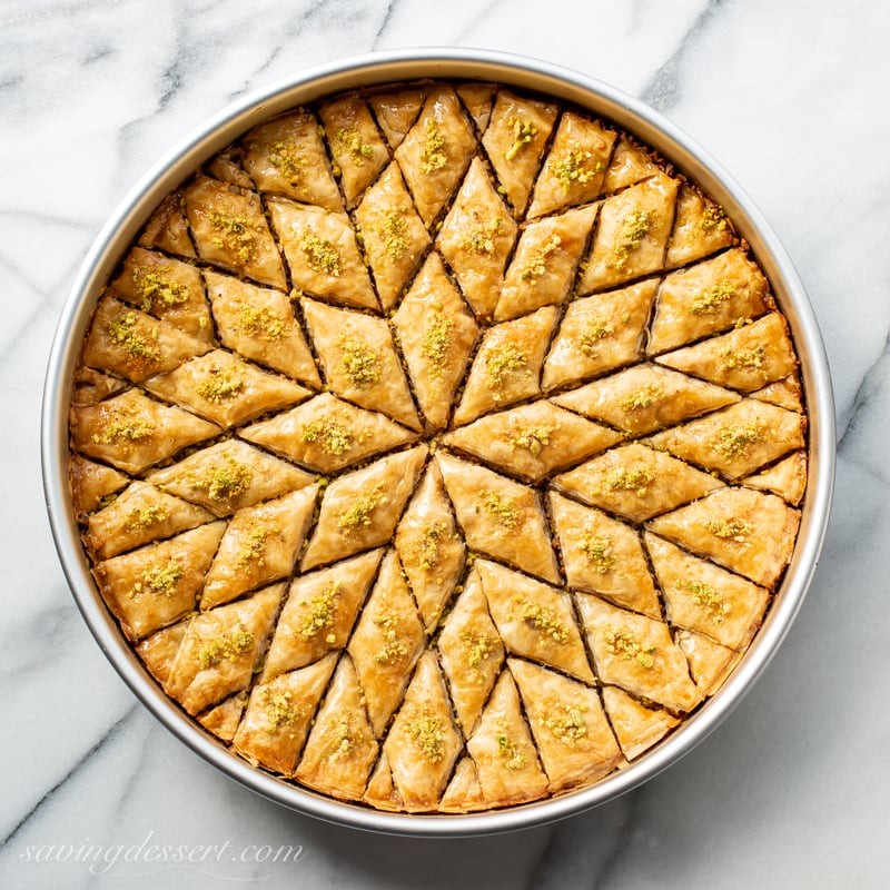 A close-up shot of a golden-brown, flaky baklava with honey dripping down, garnished with chopped nuts.