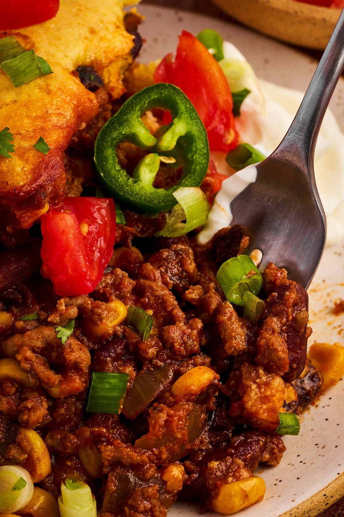 Delicious chili loaded beef skillet garnished with cheese and green onions, served with cornbread