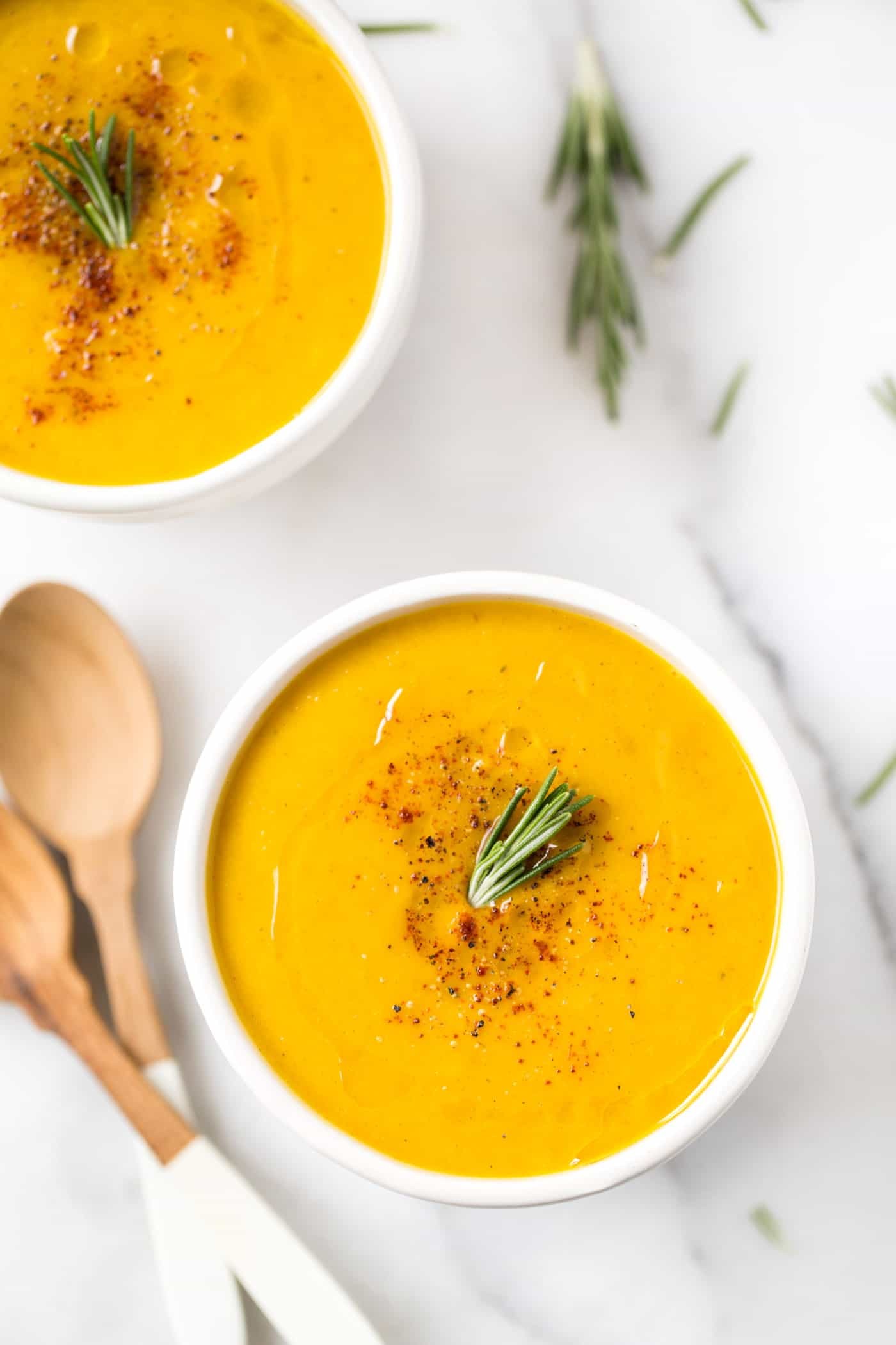 A rustic bowl of butternut squash and apple soup garnished with cinnamon and a sprig of rosemary