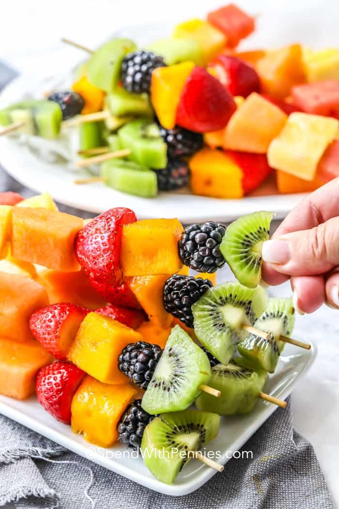 Close-up of colorful fruit kebabs on a rustic wooden table with a glass of lemonade