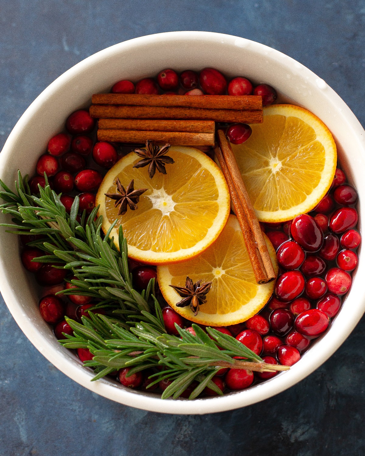 Cozy Christmas simmer pot with oranges, cranberries, cinnamon sticks, steam rising, warm lighting