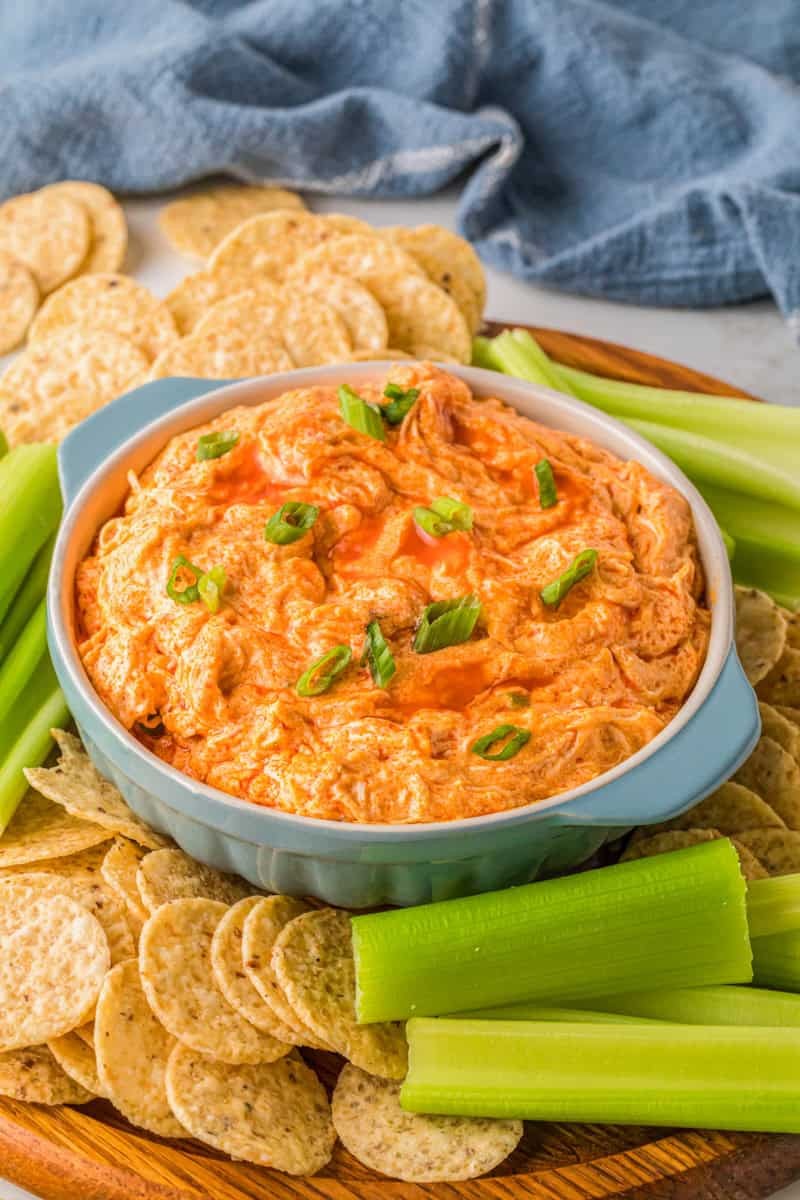Creamy buffalo chicken dip in a serving dish with tortilla chips and celery sticks, vibrant orange color, party atmosphere