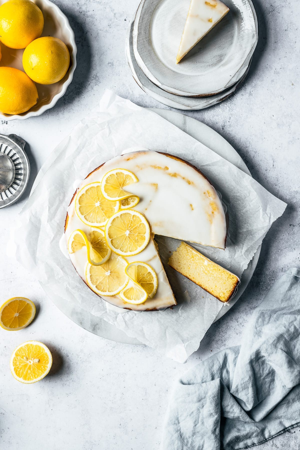 A rustic, home-baked lemon and almond cake, dusted with powdered sugar, and garnished with lemon slices and almond slivers.