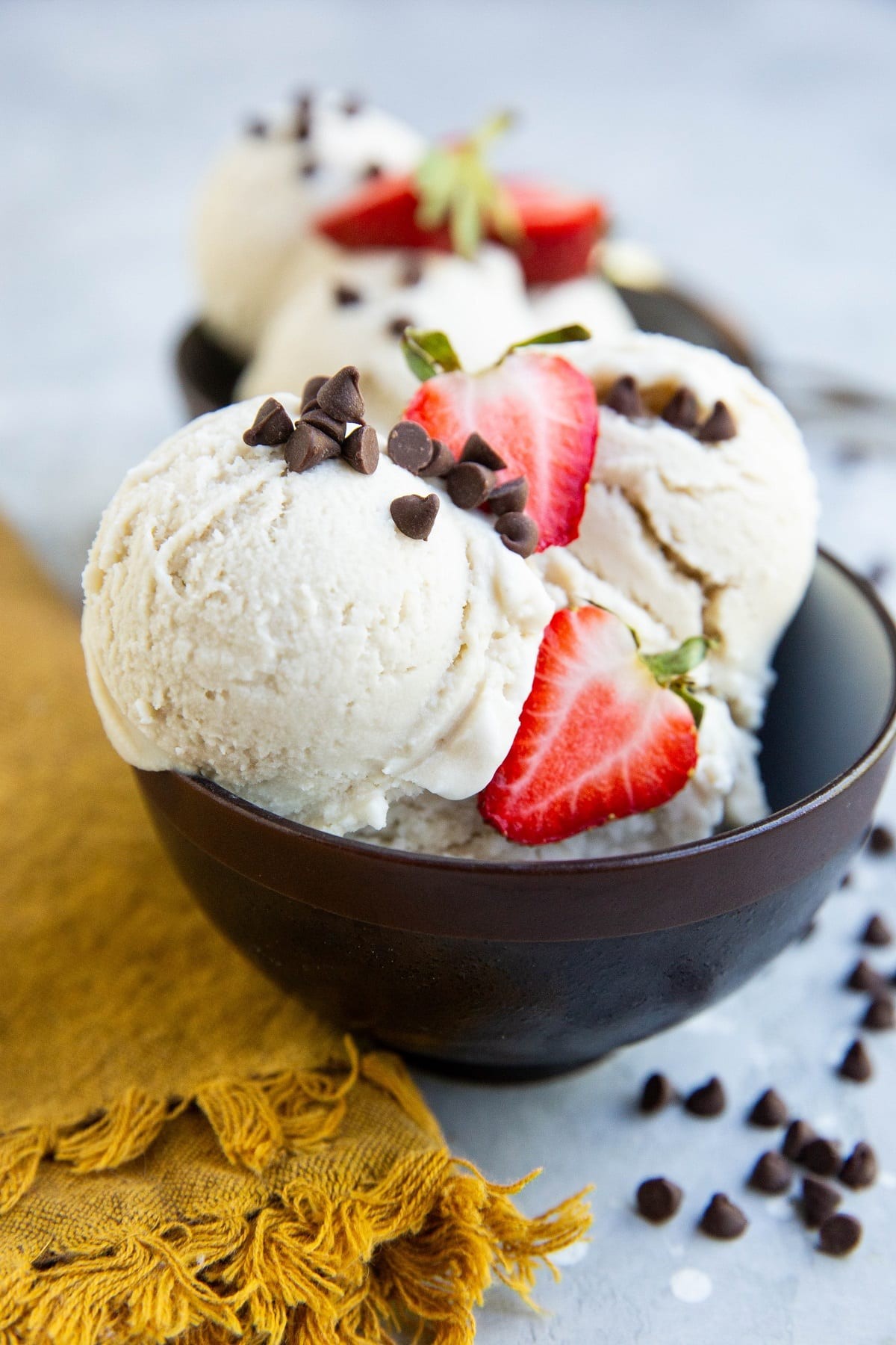 Three scoops of vegan vanilla ice cream in a bowl with fresh berries