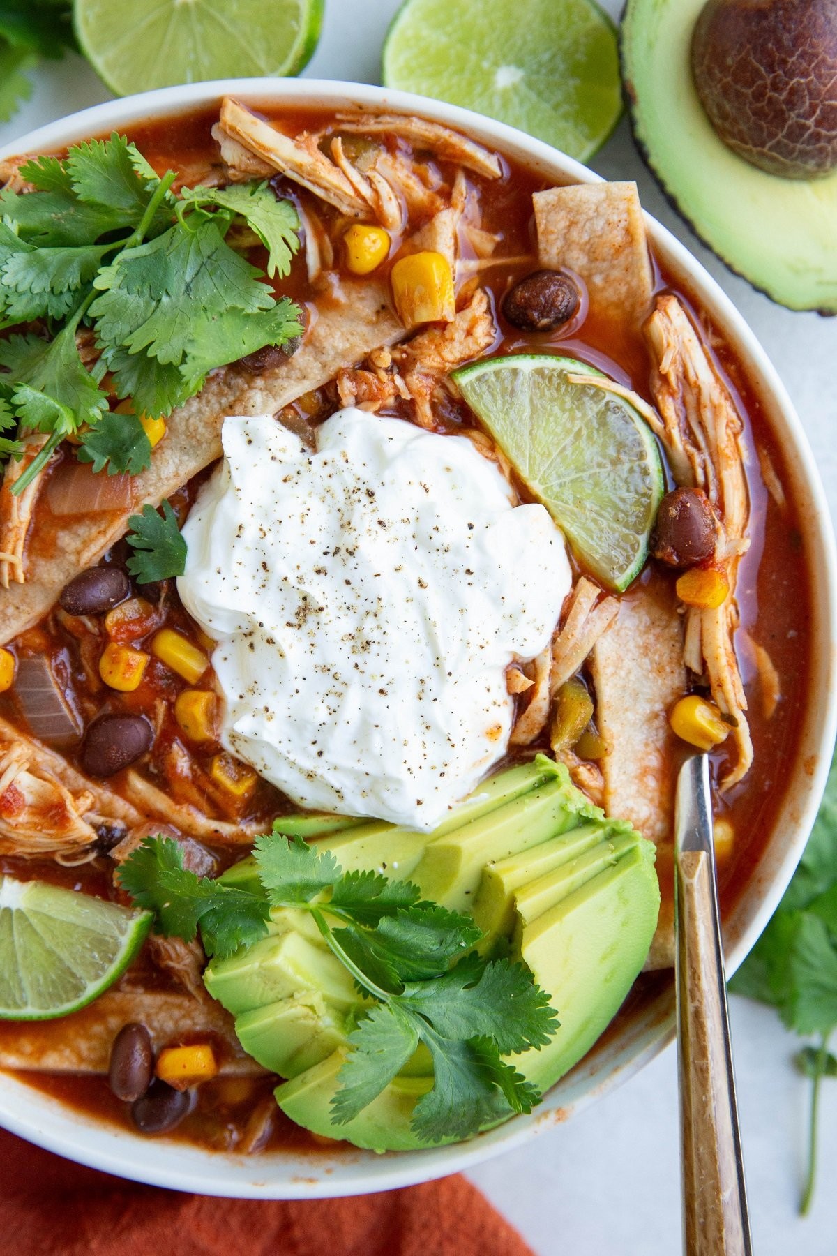A large bowl of King-Sized Chicken Tortilla Soup, garnished with avocado, sour cream, and tortilla strips