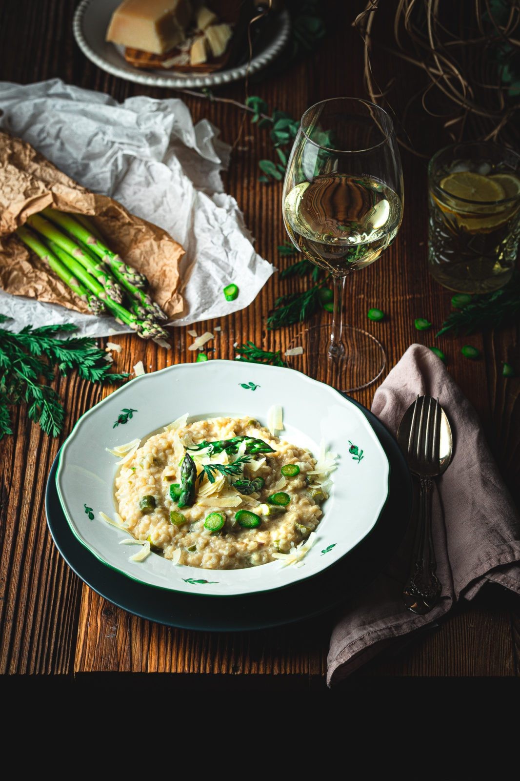 A rustic wooden table set with a bowl of creamy asparagus risotto, garnished with fresh rosemary sprigs