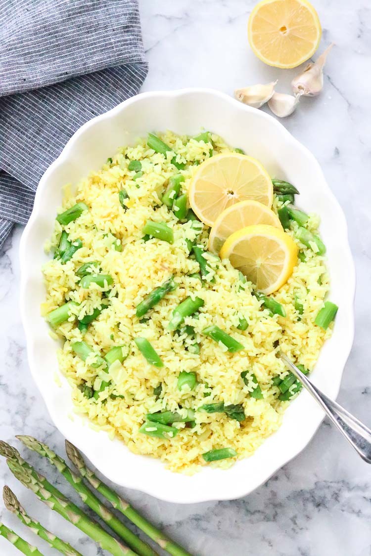 A bowl of fluffy steamed rice topped with bright green steamed asparagus spears and a squeeze of lemon juice.