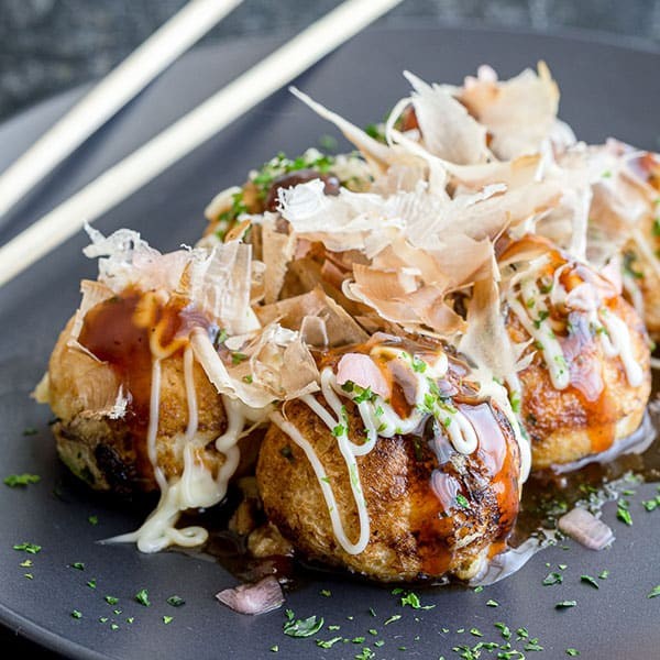 Golden-brown takoyaki balls on a plate, garnished with bonito flakes, takoyaki sauce, mayonnaise, and green onions