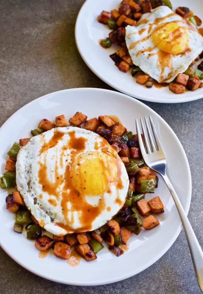 Sweet potato rice hash topped with a fried egg and a drizzle of chipotle aioli, shot in a rustic kitchen setting.