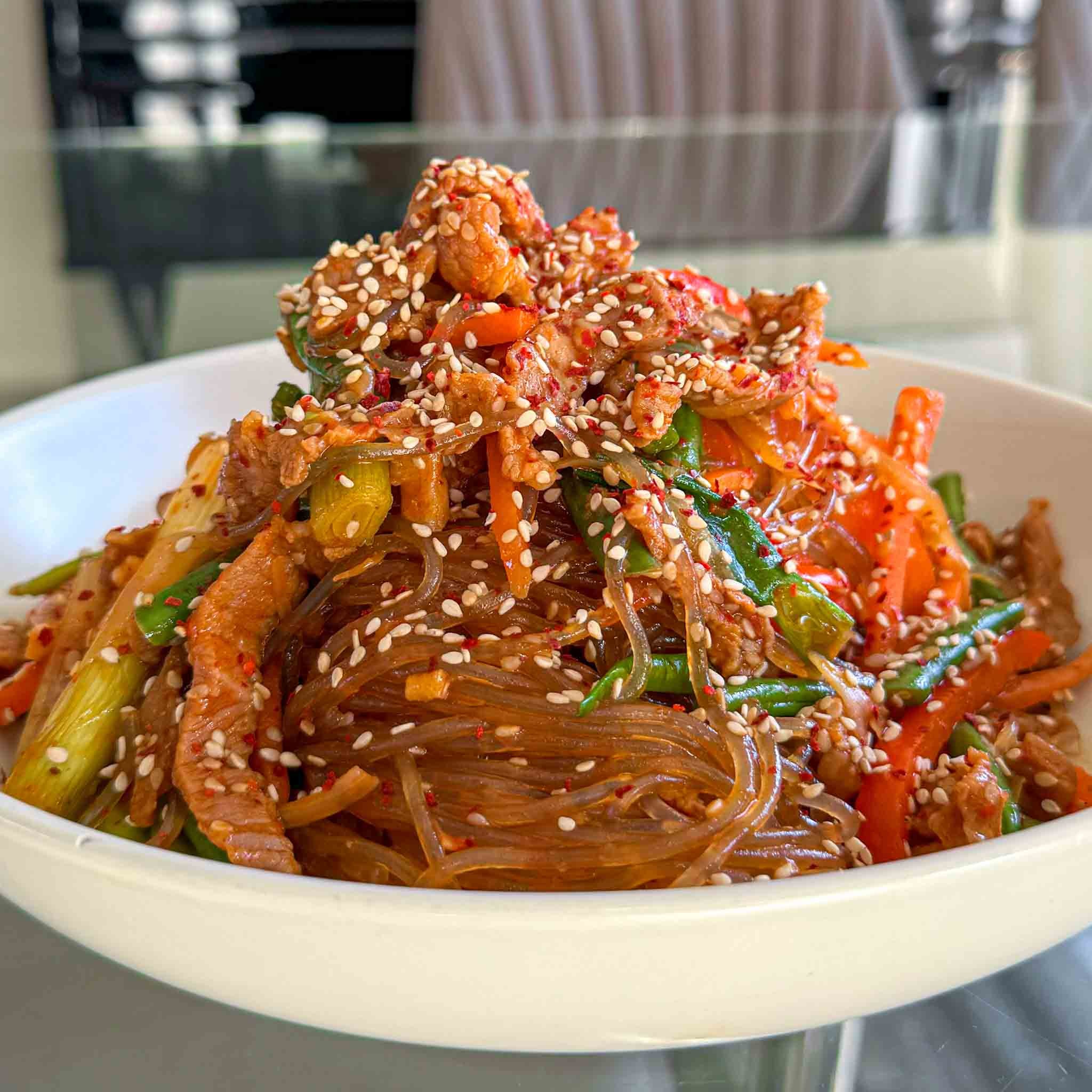 A vibrant, close-up shot of a delicious Spicy Asian Noodle dish, showing the noodles, pork, vegetables, and sauce