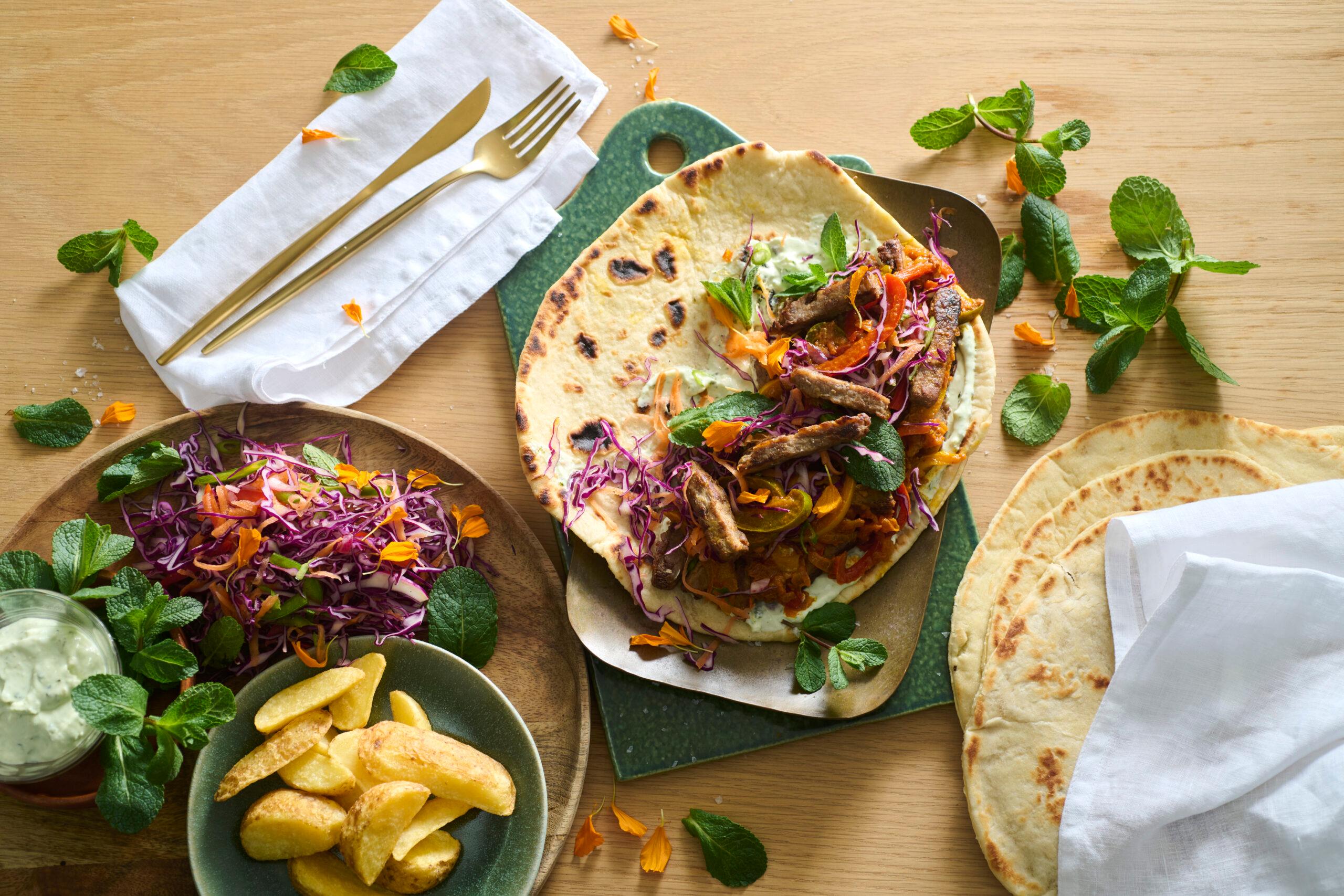 A person taking a bite of a roti with roasted vegetables and tahini dressing, a happy expression on their face