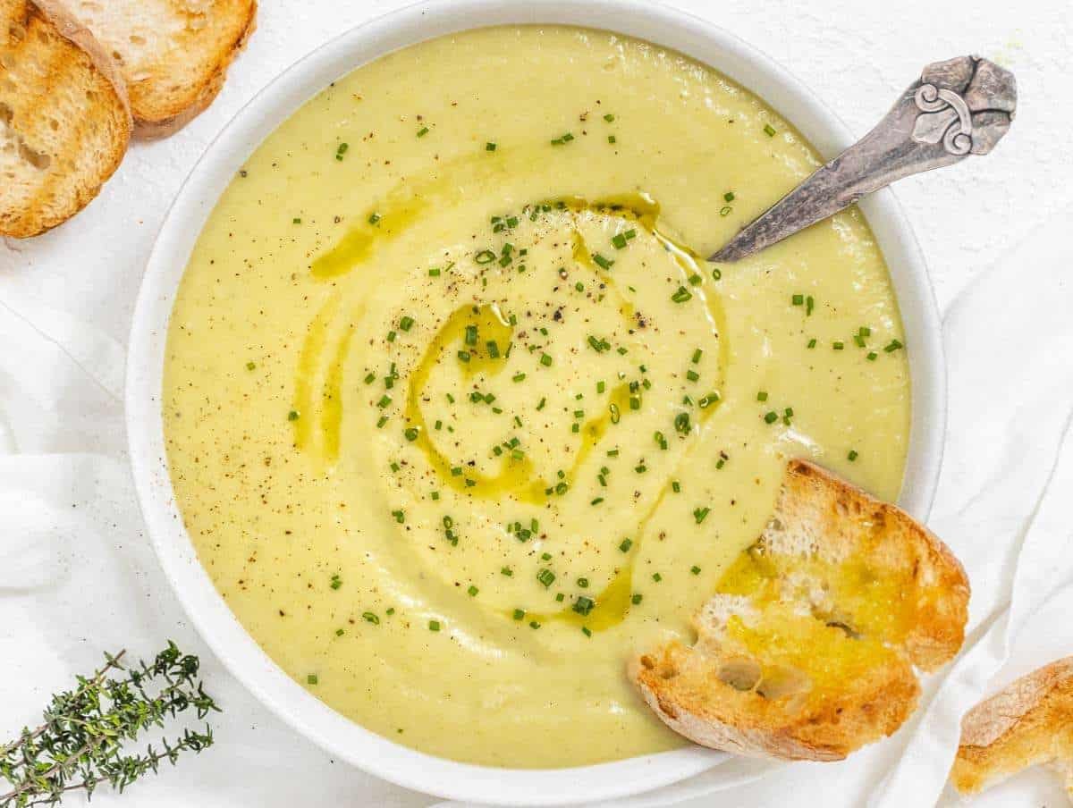 Rustic creamy potato leek soup in a bowl with crusty bread, garnished with chives