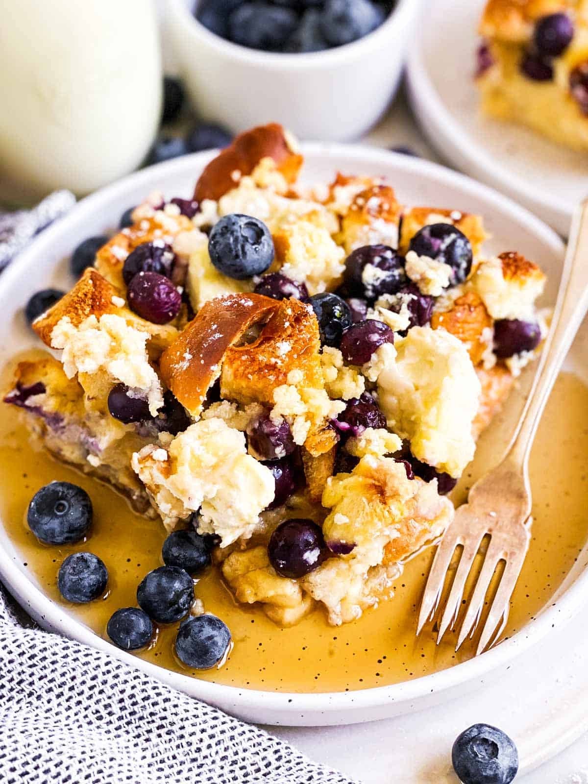 Overhead shot of baked blueberry french toast casserole with a golden brown streusel topping, fresh blueberries, and a drizzle of maple syrup, cozy breakfast setting
